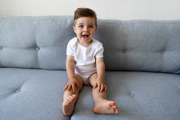 Engraçado criança feliz e saudável de um ano de idade, sentada no sofá em casa, lindos olhos, crianças brincam e criança ...