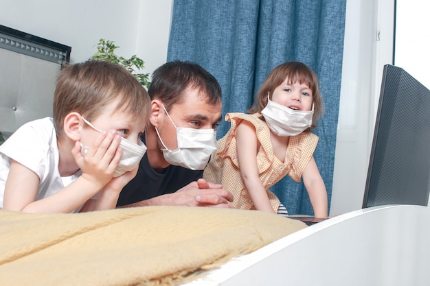 Engraçado crianças menino e menina e seu pai na máscara médica está sentado em casa em quarentena.