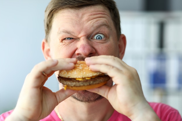 Engraçado homem barbudo com expressão facial idiota comendo hambúrguer grande