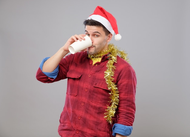 Engraçado jovem bêbado usando chapéu de papai noel segurando um copo de papel