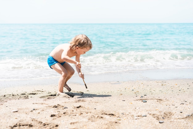 Engraçado menino bonitinho brincando com areia na costa do mar verão praia férias infância estilo de vida holi ...