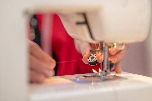 Foto enhebrar máquina de coser. manos sosteniendo bobina con hilo preparando máquina de coser para coser en atelier sin rostro