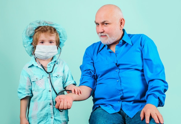 Enkel in medizinischer Maske spielt Arzt mit Opa. Medizin. Notfall. Behandlung zu Hause.