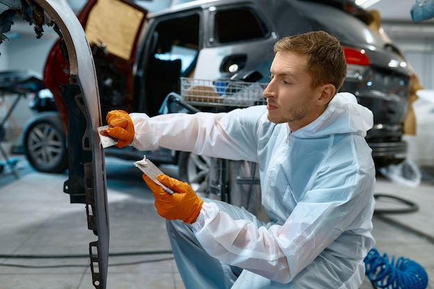 Enmasillado mecánico o enyesado de carrocerías de automóviles en el garaje del taller. Eliminación de arañazos y agujeros antes de pintar en el servicio del coche