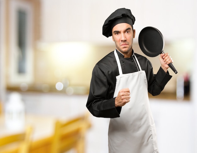 Enojado joven chef utilizando un utensilio de cocina