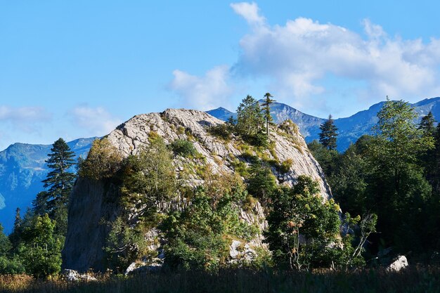 Enorme acantilado de piedra caliza independiente cubierto de árboles en un paisaje otoñal con el telón de fondo de una cordillera