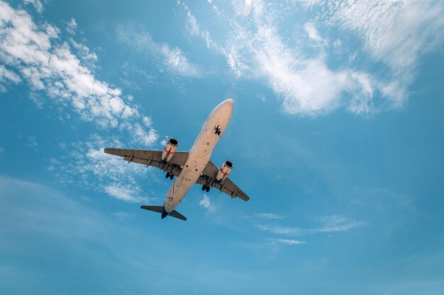 Un enorme avión comercial blanco vuela por encima de las nubes en el cielo azul, vista desde abajo