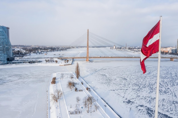 Enorme bandera de Letonia ondea en el viento con el casco antiguo de Riga al fondo en Letonia. Hermoso día de invierno.