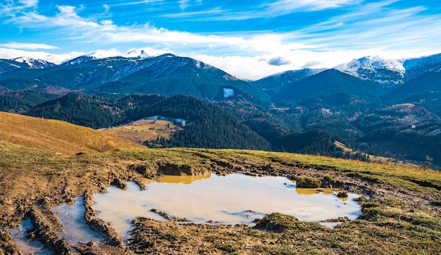 Un enorme charco de barro con barro repugnante en un pequeño sendero en las montañas de los Cárpatos contra hermosas colinas otoñales