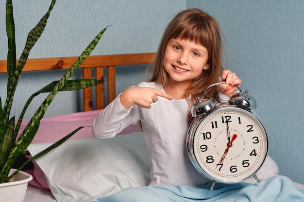 Foto enorme despertador nas mãos de uma menina de sorriso feliz no quarto 7 horas da manhã foto de alta qualidade