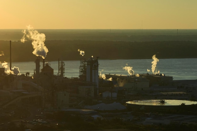 Enorme fábrica com altas chaminés poluindo a atmosfera com fumaça de dióxido de carbono do processo de produção no pátio de fabricação da planta Local industrial ao pôr do sol