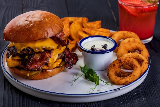 Enorme hamburguesa con aros de cebolla y salsa de ajo sobre fondo de madera negra