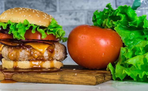 Una enorme hamburguesa jugosa está sobre una tabla de cortar con verduras sobre un fondo de ladrillo gris