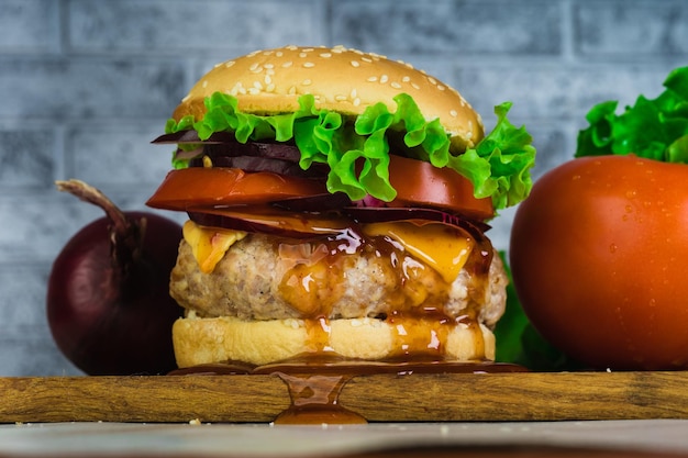 Foto una enorme hamburguesa jugosa está sobre una tabla de cortar con verduras sobre un fondo de ladrillo gris