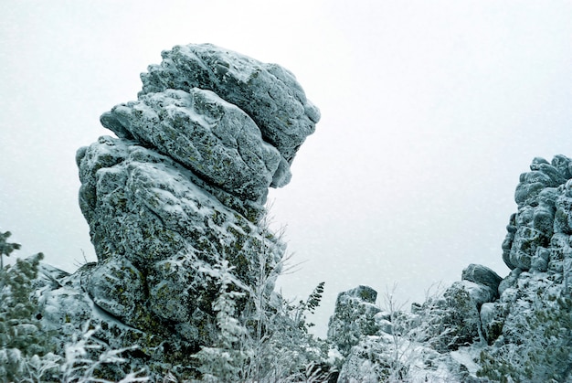 Una enorme roca helada agrietada inclinada sobre el bosque subártico contra un cielo nevado blanco