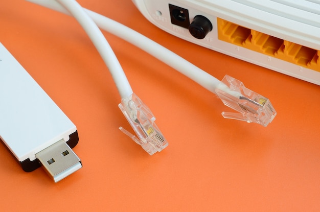 El enrutador de Internet, el adaptador USB portátil de wi-fi y los enchufes de cable de Internet se encuentran sobre un fondo naranja brillante. Artículos requeridos para la conexión a internet