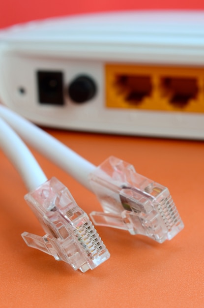 El enrutador de Internet y los enchufes de cable de Internet se encuentran sobre un fondo naranja brillante