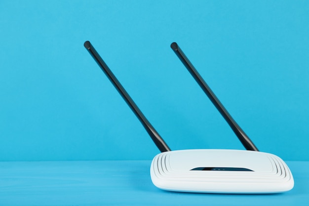 Enrutador wi-fi blanco con antenas negras sobre superficie azul con espacio de copia