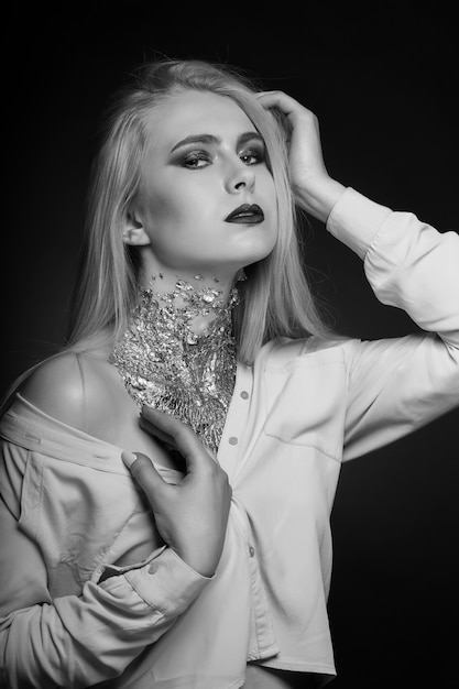 Ensaio de beleza em preto e branco: esplêndida modelo loira posando no estúdio com maquiagem brilhante e papel alumínio no pescoço
