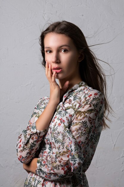 Ensaio de ensaio de uma modelo morena surpresa com cabelos esvoaçantes posando em um vestido de chiffon