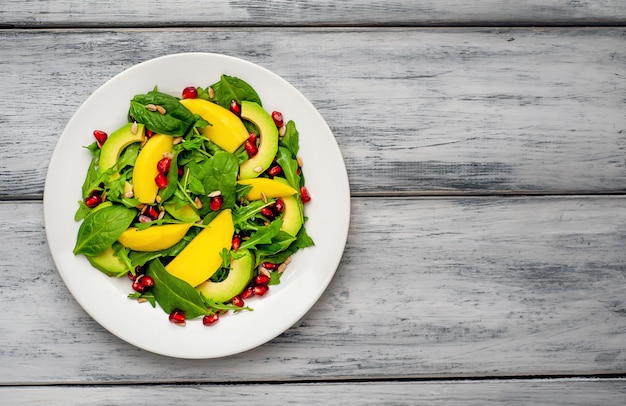 Ensalada de aguacate con espinacas y granada en un plato blanco sobre una mesa de madera