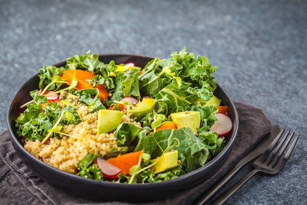 Ensalada del aguacate, de la quinoa, del ñame y de la col rizada en placa negra en un fondo oscuro.