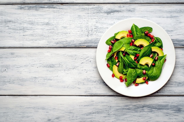 Ensalada con aguacate, rúcula, espinacas, granada, semillas sobre fondo de madera