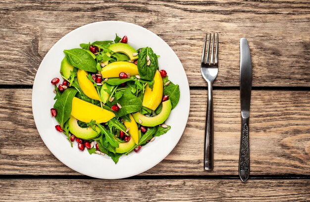 Ensalada con aguacate, rúcula, espinacas, granada, semillas sobre fondo de madera