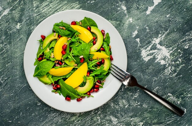 Ensalada con aguacate, rúcula, espinacas, granada, semillas sobre un fondo de piedra