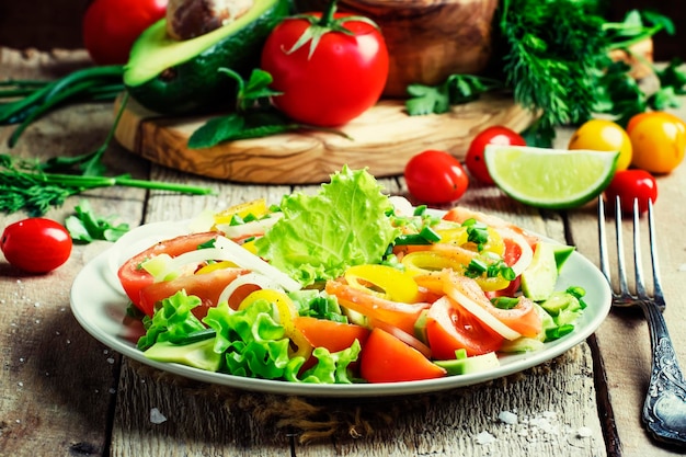 Ensalada con aguacate, salmón, lechuga, cebollas y pimientos en un plato de madera vieja, enfoque selectivo de fondo