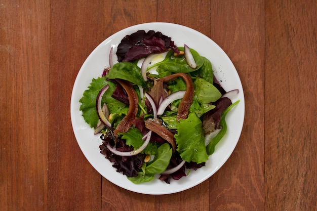 Ensalada con anchoas y cebolla en plato blanco sobre superficie marrón