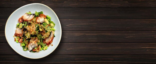 Ensalada con anguila a la parrilla y verduras en un plato sobre un fondo de madera