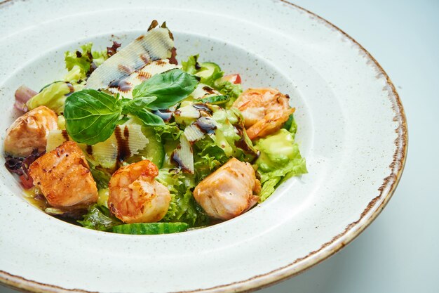 Ensalada apetitosa y saludable con camarones, lechuga de salmón, parmesano en un tazón blanco aislado en la superficie gris. Ensalada de mariscos