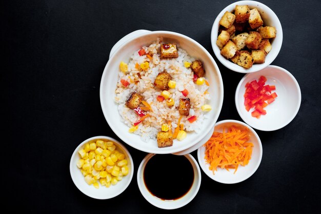 Foto ensalada de arroz vegetariano con tofu y arroz integral sobre fondo negro.