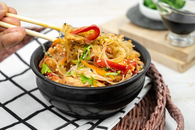 Ensalada asiática con fideos de arroz, verduras, champiñones, pollo y salsa de soja. Funchose con fideos blancos transparentes en plato negro