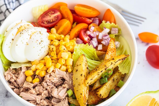 Ensalada de atún con huevos, verduras y maíz en un cuenco blanco con fondo blanco