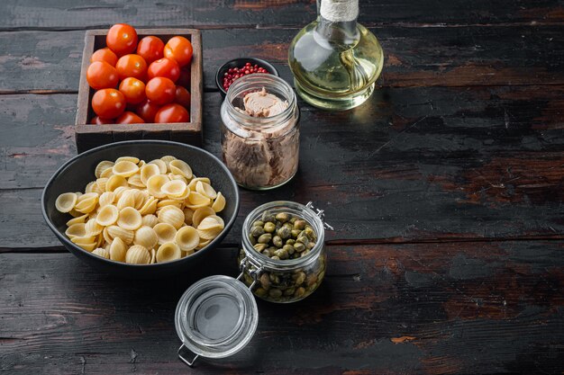 Ensalada de atún con ingredientes de pasta y verduras, sobre mesa de madera oscura.