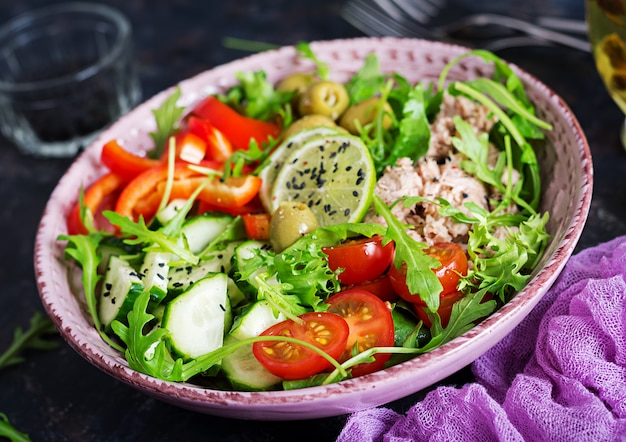 Ensalada de atún con tomate, aceitunas, pepino, pimiento dulce y rúcula sobre fondo rústico