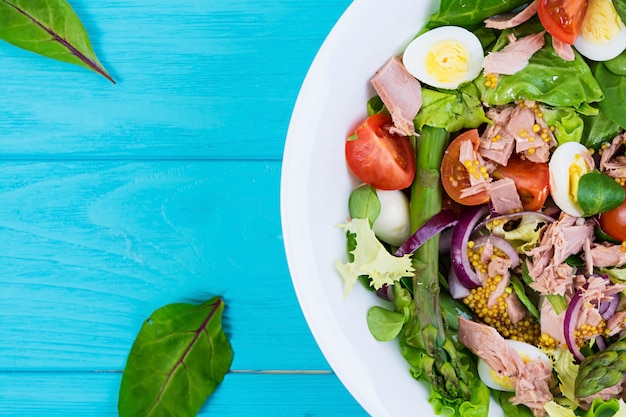 Ensalada de atún, tomate, codorniz, espárragos y cebolla en madera