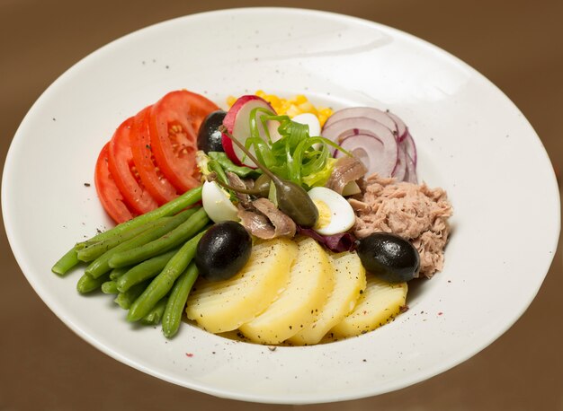 Ensalada de atún con verduras, colocada en un plato blanco, fondo marrón