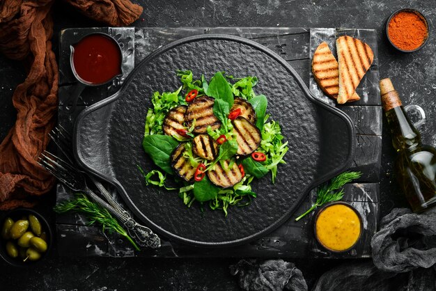 Ensalada de berenjena espinacas y repollo en un plato negro Comida vegana Vista superior Estilo rústico