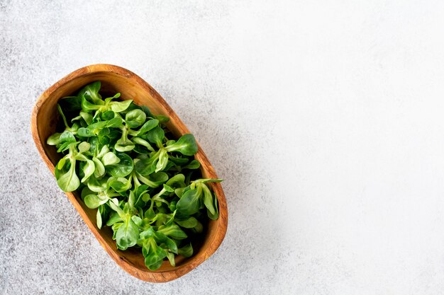 Ensalada de berro fresca cruda en cuenco de madera de oliva sobre una mesa de piedra ligera.