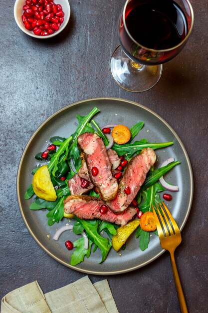 Ensalada de bife de ternera a la plancha con rúcula, patatas, zanahorias, cebollas y granada. Alimentación saludable. Dieta.