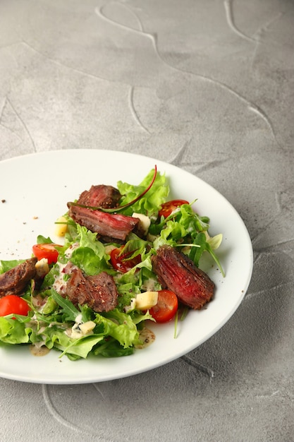 Ensalada de bistec con tomates cherry y queso en un plato blanco sobre una mesa de hormigón