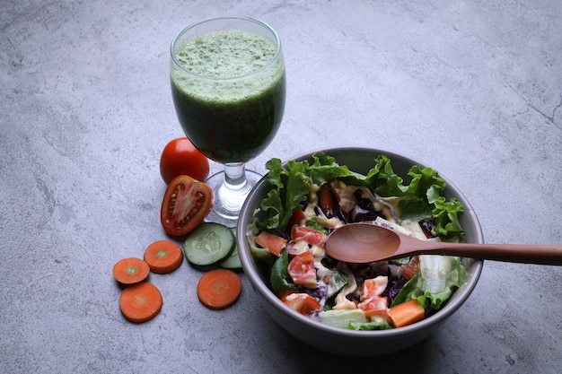 Ensalada en el bol con cuchara de madera con jugo de vegetales verdes en el vaso