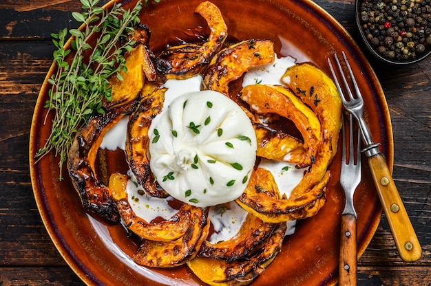 Ensalada con Burrata de Queso y calabaza al horno en un plato. Fondo de madera oscura. Vista superior.