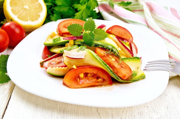 Ensalada de calabacín joven, rábano, tomate y menta aromatizada con jugo de limón y salsa de soja en un plato, servilleta sobre un fondo de tabla de madera clara