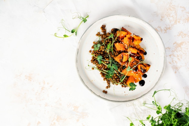 Ensalada con calabaza al horno, lentejas y aderezo balsámico adornado con microgreens de guisantes en una luz