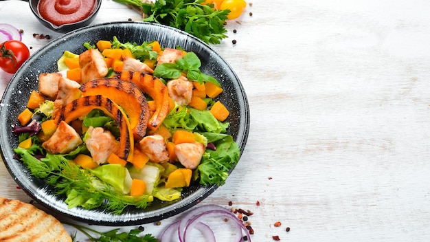 Ensalada de calabaza con carne de pollo y verduras en un plato negro sobre un fondo blanco de madera Vista superior Espacio libre para el texto