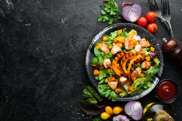 Ensalada de calabaza con carne de pollo y verduras en un plato negro sobre fondo negro Vista superior Espacio libre para el texto